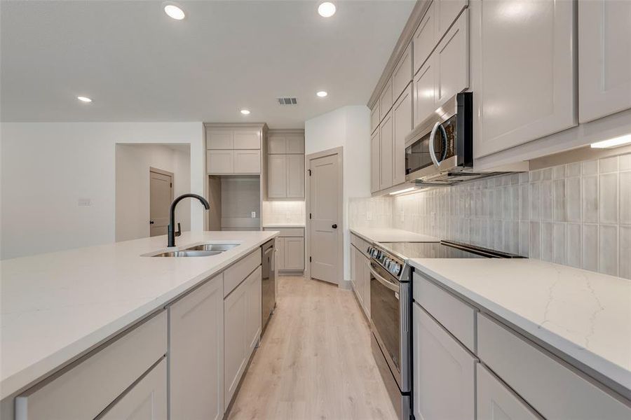 Kitchen featuring sink, appliances with stainless steel finishes, light stone countertops, decorative backsplash, and light wood-type flooring