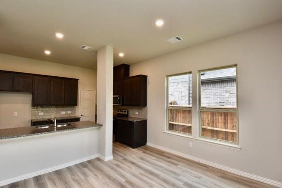 Kitchen with tasteful backsplash, light stone counters, stainless steel microwave, light wood-type flooring, and recessed lighting Kitchen with tasteful backsplash, light stone counters, stainless steel microwave, light wood-type flooring, and recessed lighting