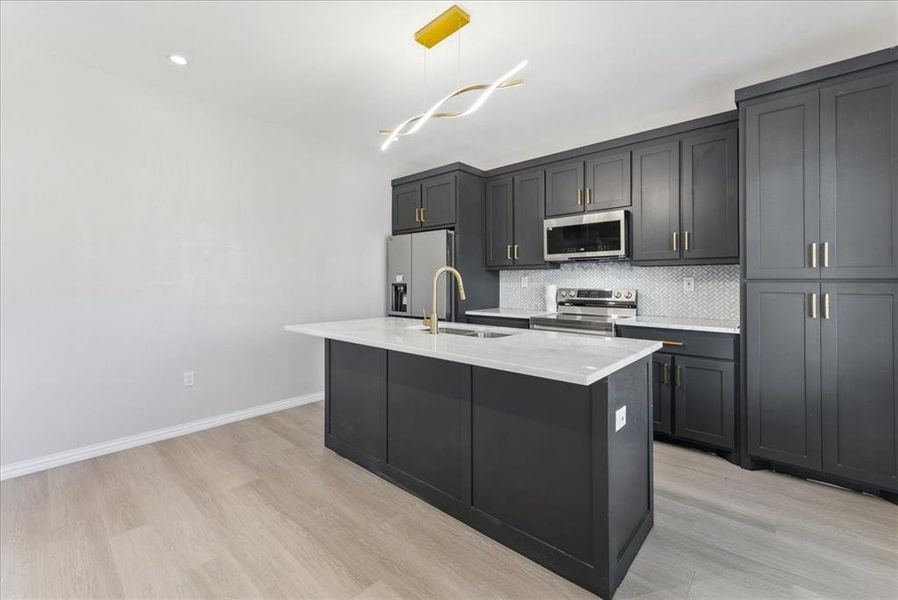 Kitchen featuring a center island with sink, backsplash, appliances with stainless steel finishes, a sink, and light wood-type flooring