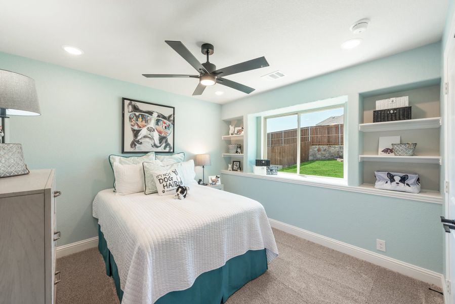 Bedroom with light blue walls, ceiling fan, built-in shelves, and a window overlooking a backyard