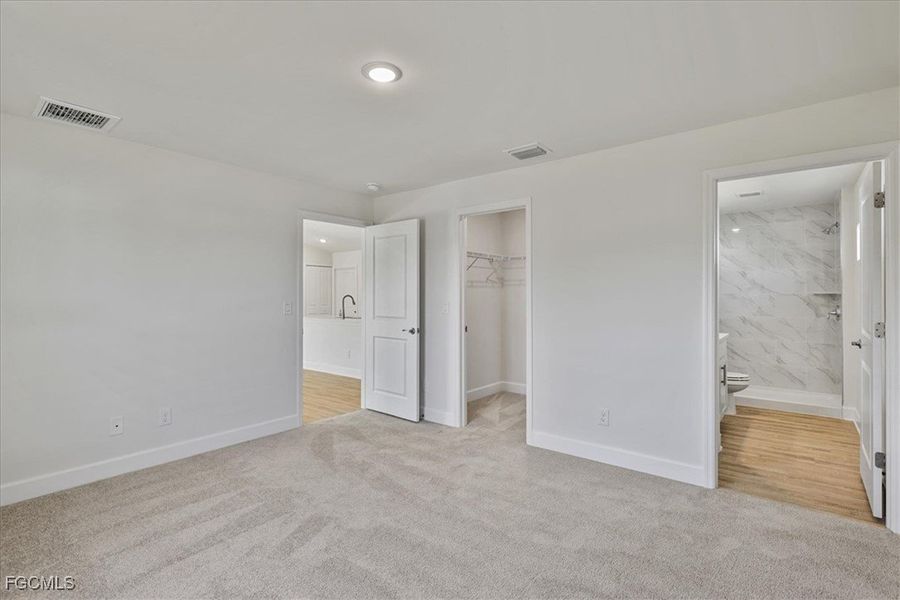 Unfurnished bedroom featuring a walk in closet, light colored carpet, and ensuite bath