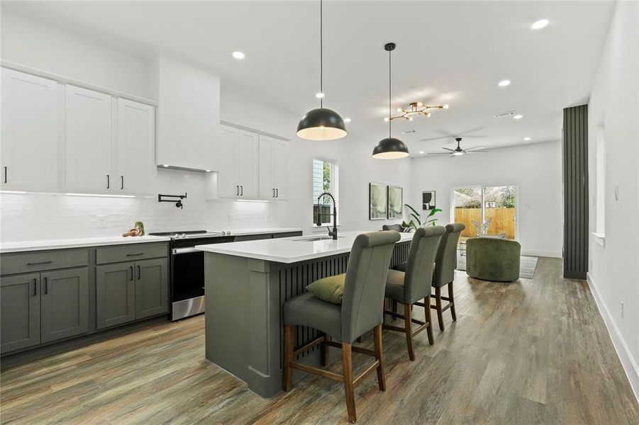 Dual tone kitchen with two tone cabinetry, electric stove, light wood-style floors, backsplash, and an island with sink