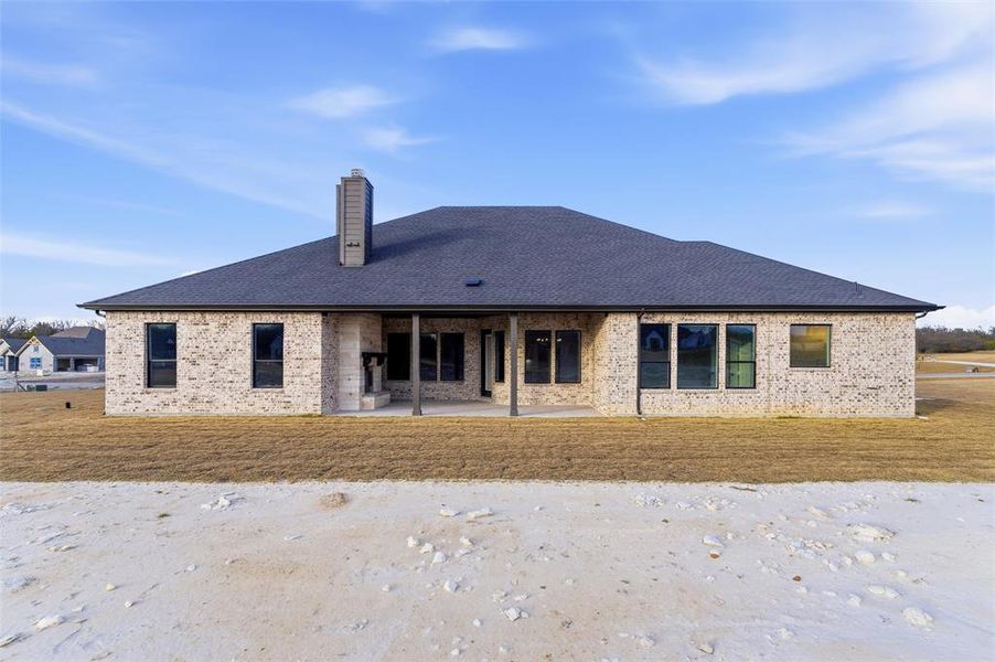 Back of property featuring a patio area, brick siding, a chimney, and roof with shingles