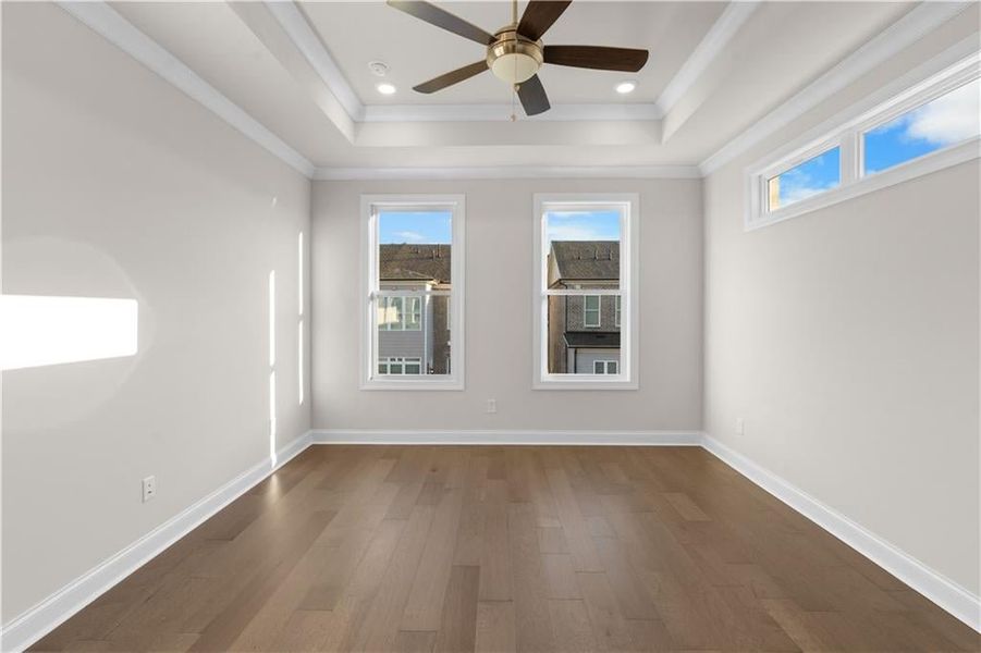 Unfurnished room with dark wood-type flooring, healthy amount of natural light, ornamental molding, a ceiling fan, and a raised ceiling