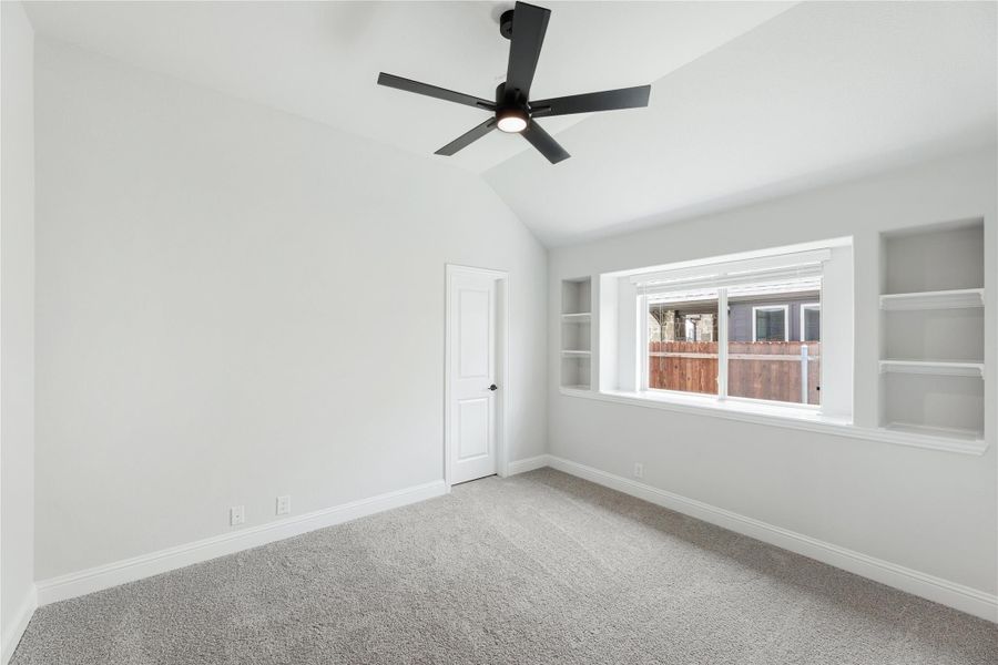 Empty bedroom with vaulted ceiling, black ceiling fan, built-in shelves, and carpet flooring