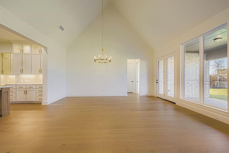 Unfurnished dining area with high vaulted ceiling, a chandelier, and light wood finished floors