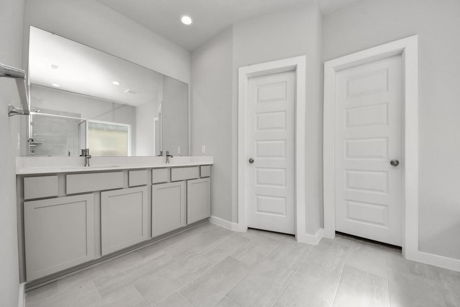 Elevate your daily routine at the elegant vanity, now equipped with double sinks, light countertops, modern hardware, and beautiful recessed lights. Sample photo of completed home with similar floor plan. Actual colors and selections may vary.