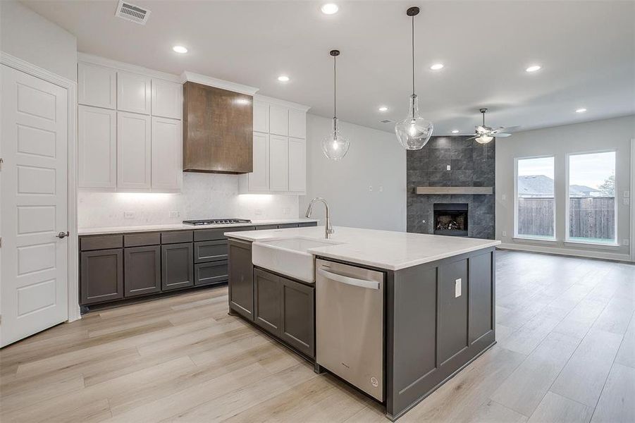 Kitchen featuring custom exhaust hood, pendant lighting, dishwasher, white cabinetry, and an island with sink