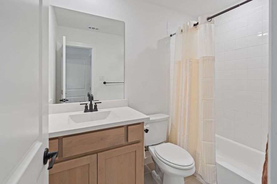Bathroom featuring a light wood-finish vanity with an integrated sink and white countertop, black fixtures, and a white tiled shower-tub combination Bathroom featuring a light wood-finish vanity with an integrated sink and white countertop, black fixtures, and a white tiled shower-tub combination