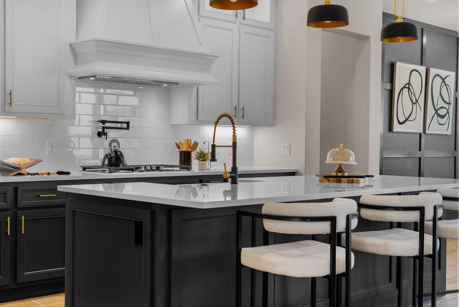 A contemporary kitchen showcasing a sleek island with seating, a gold-accented faucet, and striking pendant lights.