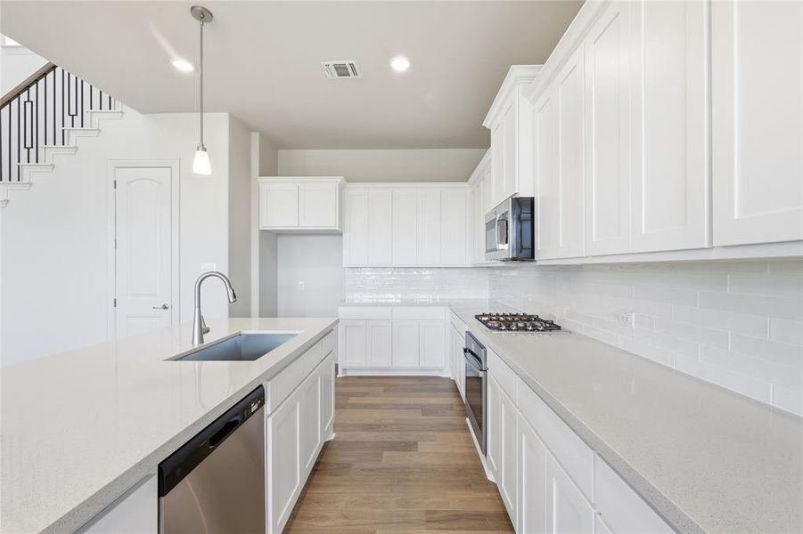 Kitchen featuring white cabinets, dark wood-type flooring, stainless steel appliances, light stone counters, and pendant lighting
