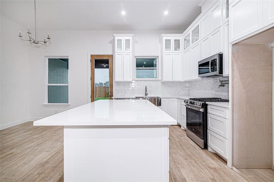 Kitchen with stainless steel appliances, light wood-type flooring, a center island, backsplash, and light countertops Kitchen with stainless steel appliances, light wood-type flooring, a center island, backsplash, and light countertops