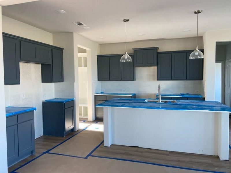 Modern kitchen featuring dark cabinetry, a central island with a sink, two pendant lights, recessed ceiling lights, and wood-finish flooring