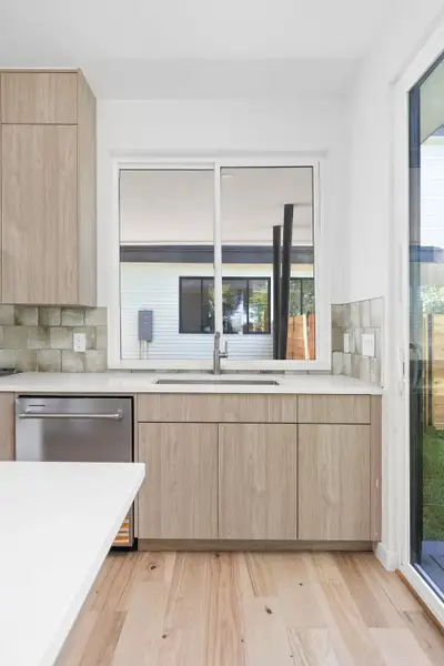 Kitchen with light brown cabinetry, a sink, modern cabinets, dishwasher, and light countertops