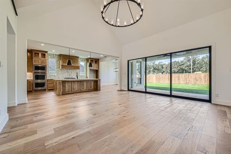 Unfurnished living room featuring light hardwood / wood-style floors, a notable chandelier, high vaulted ceiling, and sink