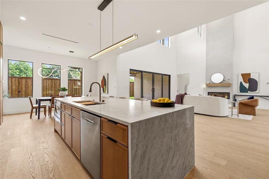 Open-concept kitchen featuring an oversized island with waterfall stone countertop, integrated stainless steel appliances, and wood-finish cabinetry