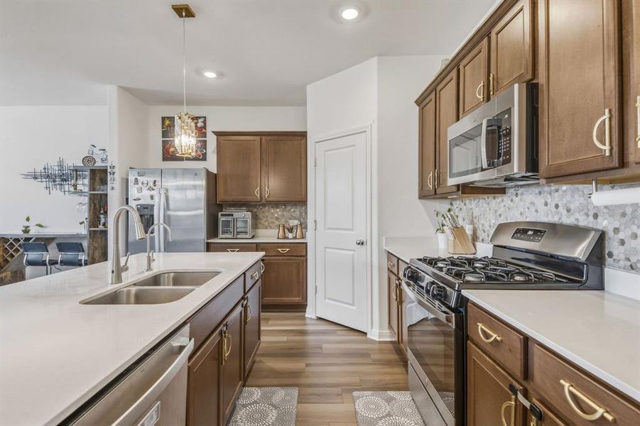 Kitchen featuring a large island with an undermount double sink, wood-finish flooring, recessed lighting, and stainless steel appliances Kitchen featuring a large island with an undermount double sink, wood-finish flooring, recessed lighting, and stainless steel appliances