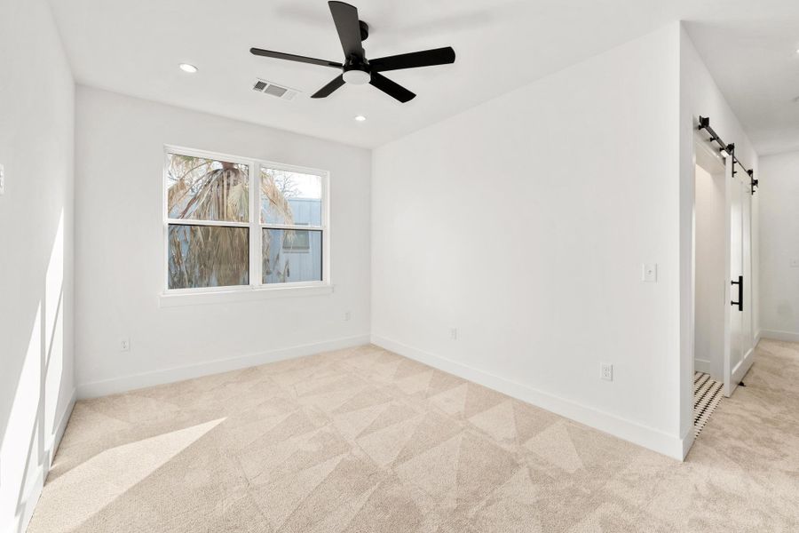 Empty room featuring a barn door, light carpet, ceiling fan, and recessed lighting