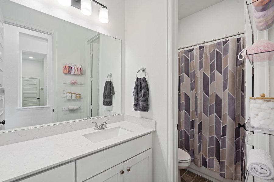 This modern bathroom features a sleek white vanity with ample storage,and contemporary lighting. It includes a tub/shower combination curtain, with neutral tones for a clean, fresh look.