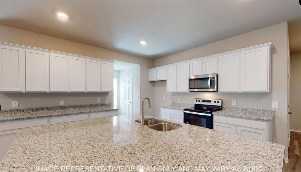 Spacious kitchen featuring an expansive island with a dual basin stainless steel sink, abundant white cabinetry, light-toned countertops, and stainless steel appliances Spacious kitchen featuring an expansive island with a dual basin stainless steel sink, abundant white cabinetry, light-toned countertops, and stainless steel appliances