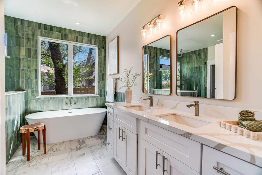 The bathroom includes a freestanding soaking tub, a large window, and a dual vanity with white cabinetry and a light-colored countertop The bathroom includes a freestanding soaking tub, a large window, and a dual vanity with white cabinetry and a light-colored countertop