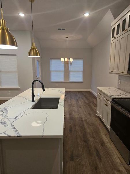 Kitchen featuring decorative backsplash, light stone countertops, electric stove, sink, and white cabinets