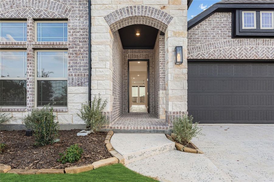 Home entrance with stone arch, brick exterior, wall sconce light, and dark two-car garage door