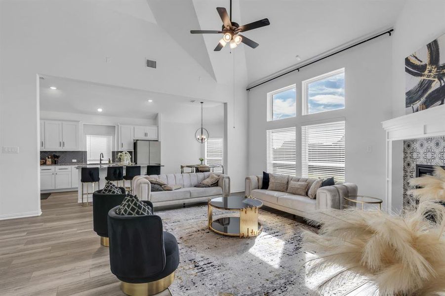 Living room with ceiling fan, high vaulted ceiling, light hardwood / wood-style floors, sink, and a fireplace