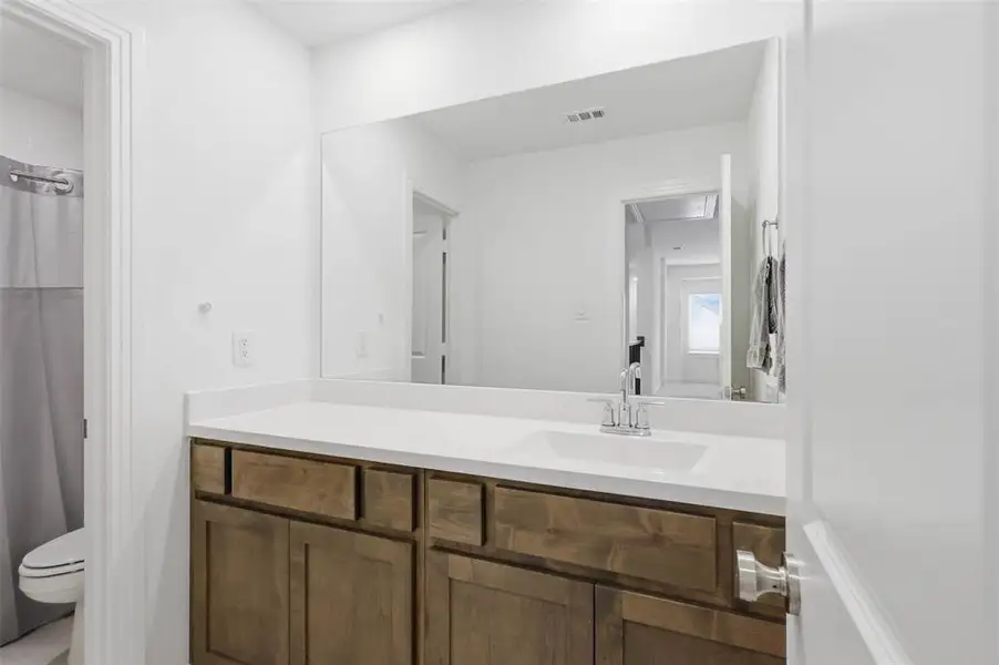 Bathroom vanity with a white countertop and integrated sink, complemented by a large frameless mirror