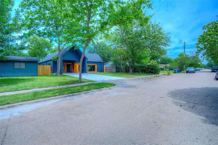 Contemporary dark blue exterior with an A-frame entry, contrasting natural wood accents, a concrete driveway, and a manicured front lawn with established trees
