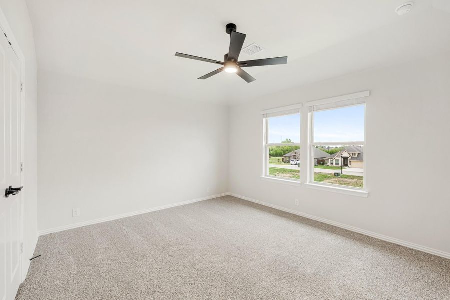 Empty bedroom with carpet flooring, ceiling fan, and double windows overlooking a neighborhood