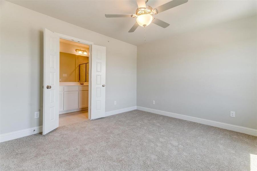 Unfurnished bedroom with light colored carpet, ceiling fan, and ensuite bath