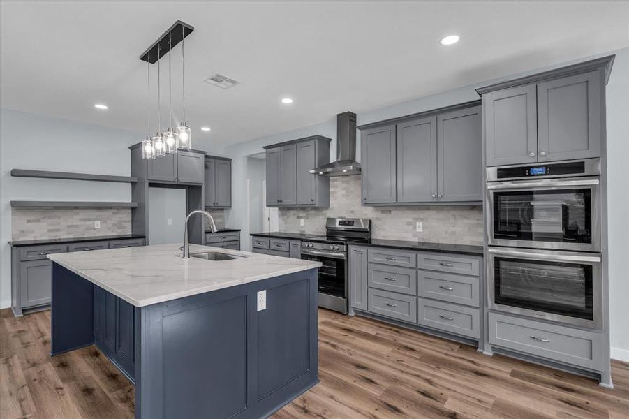 Kitchen featuring gray cabinetry, appliances with stainless steel finishes, pendant lighting, backsplash, and dark stone counters Kitchen featuring gray cabinetry, appliances with stainless steel finishes, pendant lighting, backsplash, and dark stone counters