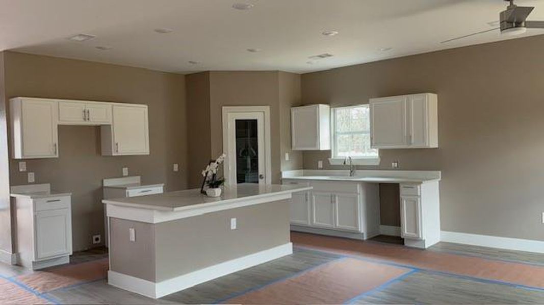 Kitchen featuring wood finished floors, baseboards, a sink, white cabinets, and a center island