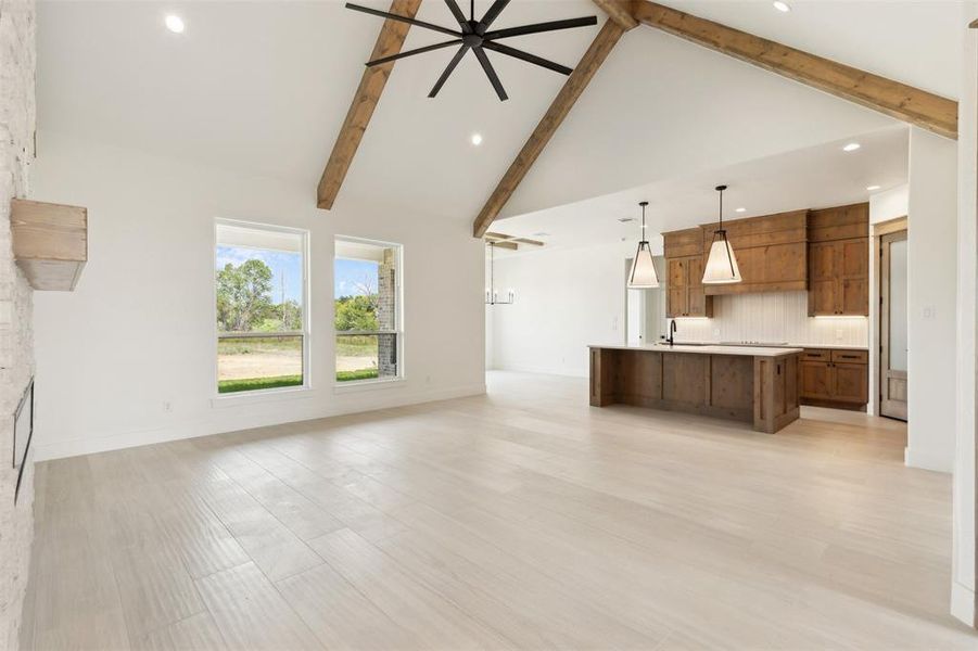 Unfurnished living room with beamed ceiling, light wood-type flooring, and high vaulted ceiling