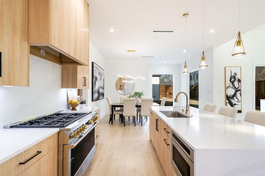 Kitchen with sink, light brown cabinets, hanging light fixtures, a kitchen island with sink, and appliances with stainless steel finishes