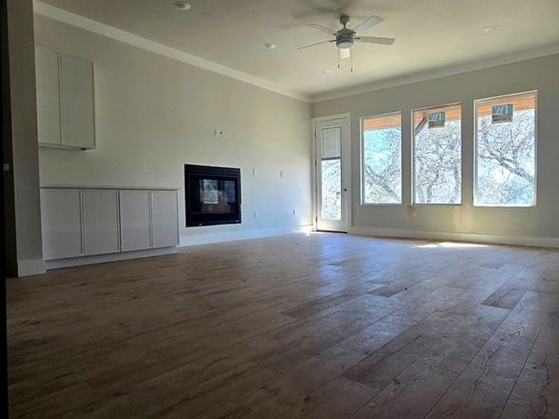Unfurnished living room featuring a glass covered fireplace, ornamental molding, hardwood / wood-style floors, and ceiling fan