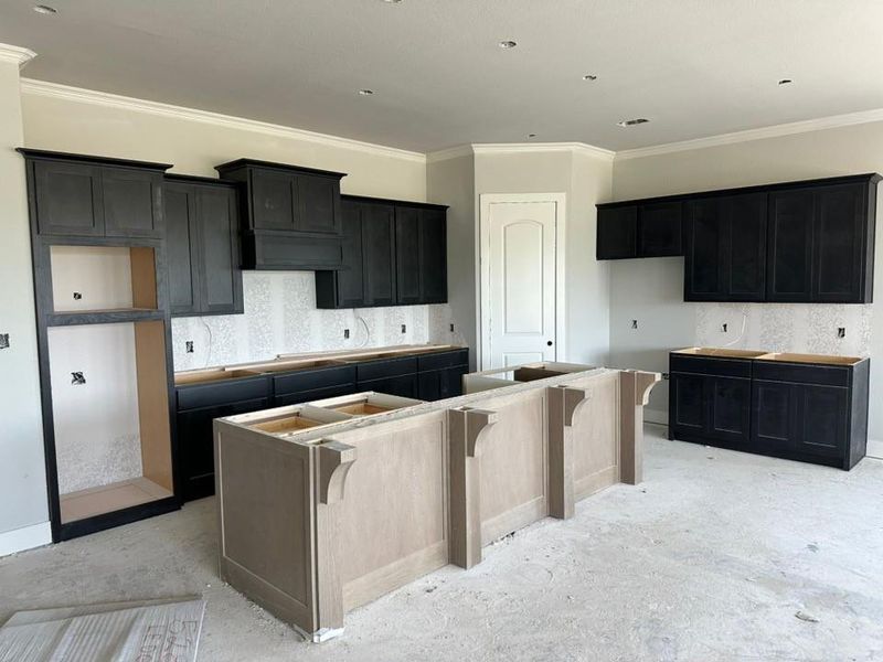 Kitchen featuring dark wood-finish cabinetry, a built-in range hood enclosure, crown molding, and recessed lighting