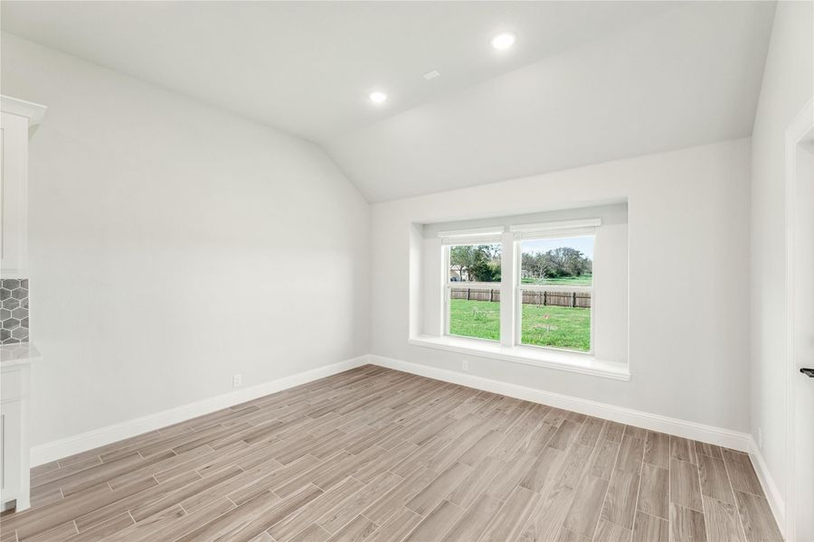 Empty room with vaulted ceiling, wood-look tile floors, and large window overlooking backyard Empty room with vaulted ceiling, wood-look tile floors, and large window overlooking backyard