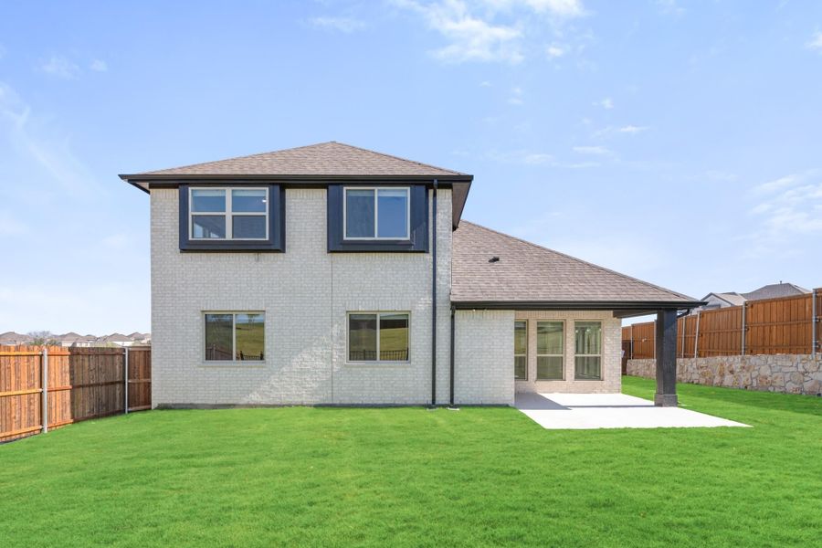 Two-story brick home rear view with covered patio, concrete pad, and fenced backyard with green lawn