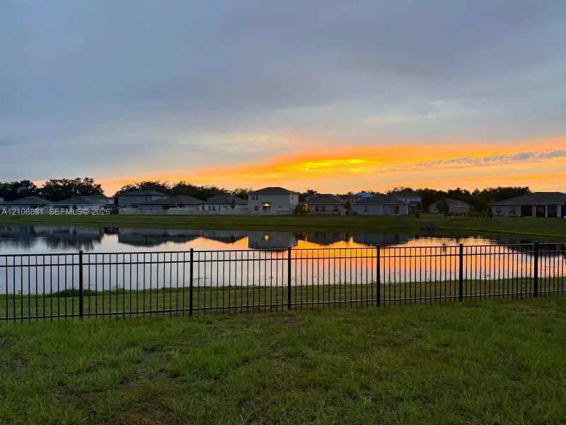 Waterfront lot featuring a black metal perimeter fence and a grass lawn, set against a backdrop of a reflective body of water