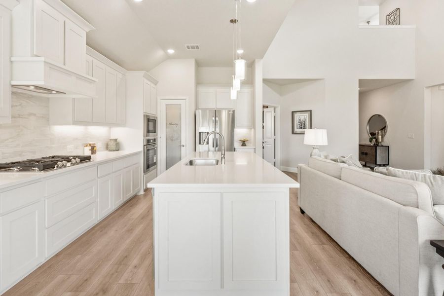 Open kitchen with white cabinets, large center island, and hardwood floors opening to living room Open kitchen with white cabinets, large center island, and hardwood floors opening to living room