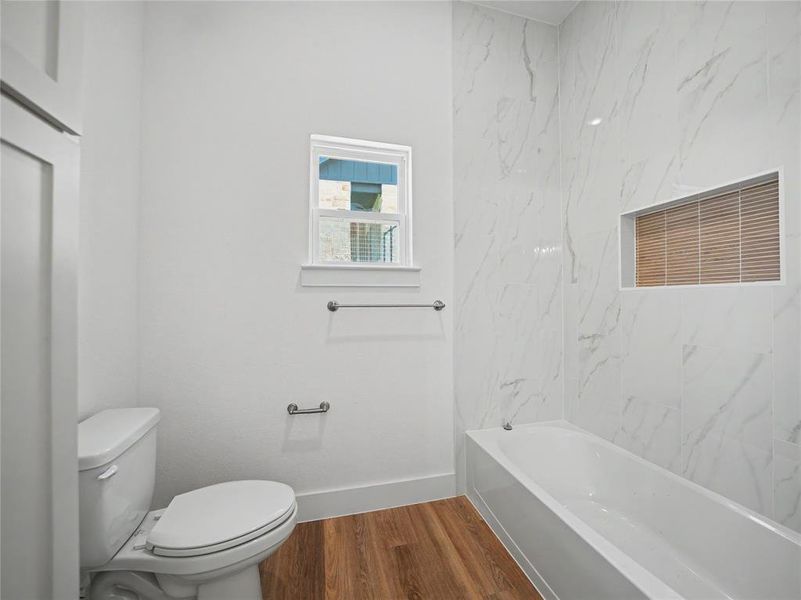 Bathroom featuring a built-in tub, white subway tile surround with a recessed niche, wood-finish flooring, and a window