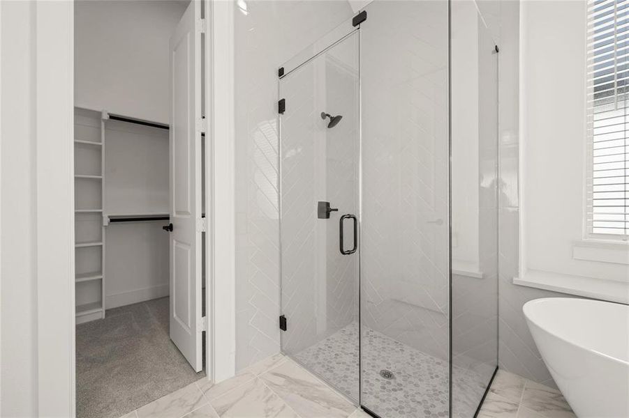 Full bathroom featuring a walk in closet, a shower stall, a soaking tub, and light marble finish flooring