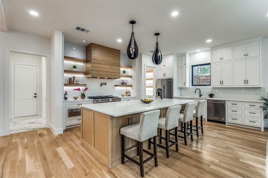 Kitchen featuring tasteful backsplash, custom range hood, stainless steel appliances, a kitchen island with sink, and white cabinetry