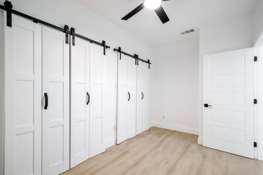 Unfurnished bedroom featuring a barn door, light wood-style flooring, and ceiling fan