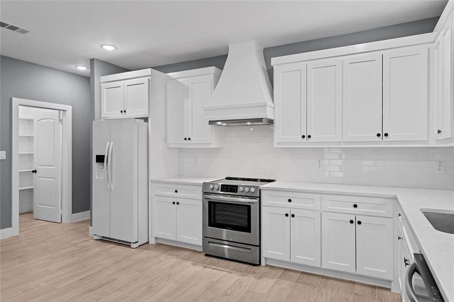 Kitchen with white refrigerator with ice dispenser, custom range hood, stainless steel electric range, white cabinetry, and recessed lighting Kitchen with white refrigerator with ice dispenser, custom range hood, stainless steel electric range, white cabinetry, and recessed lighting
