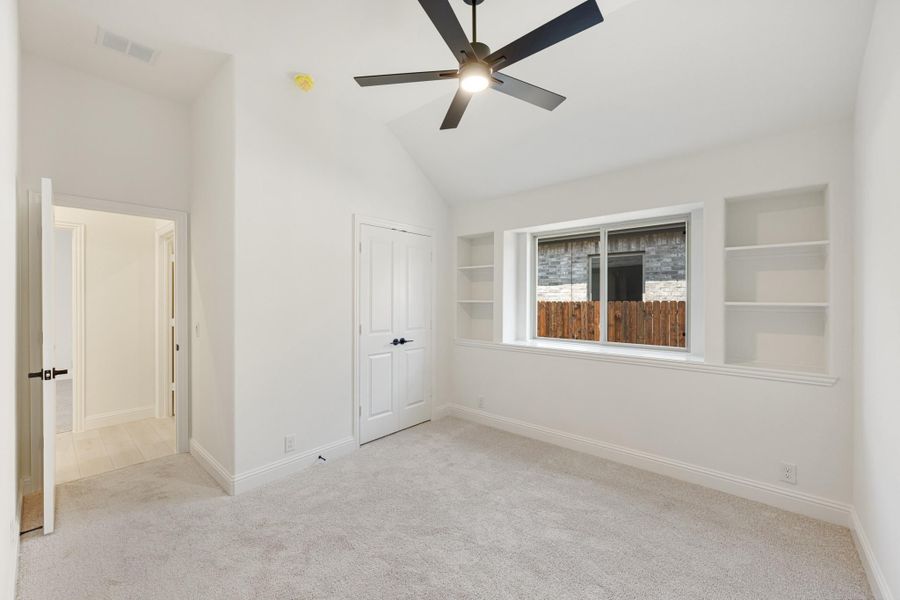 Empty bedroom with vaulted ceiling, ceiling fan, built-in shelves, and carpet flooring