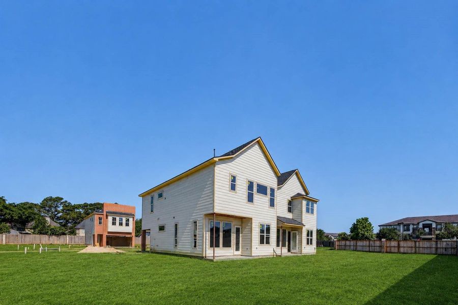 Wide rear-side exterior view capturing the two-story profile, light siding, rear doors, window placement, and expansive lawn area. This perspective emphasizes the home’s modern new-construction design, outdoor space, and neighborhood layout, while showing how the homes are positioned within the developing boutique community. Wide rear-side exterior view capturing the two-story profile, light siding, rear doors, window placement, and expansive lawn area. This perspective emphasizes the home’s modern new-construction design, outdoor space, and neighborhood layout, while showing how the homes are positioned within the developing boutique community.