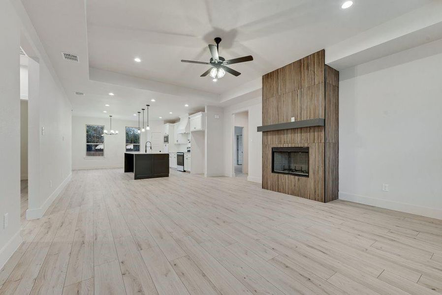 Unfurnished living room with recessed lighting, light wood-style floors, a fireplace, a ceiling fan, and a raised ceiling